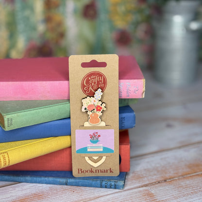 Bookmark with floral design on a cardboard backing, placed on a stack of colorful books.